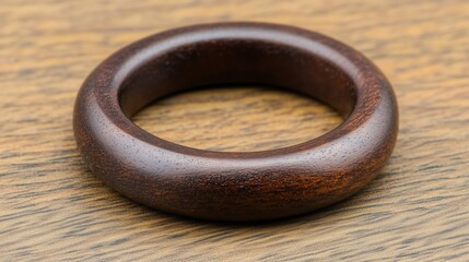 A detailed close-up of a handcrafted wooden ring with a smooth, dark ebony finish, resting on a natural wood-textured background, showcasing elegance and artisanal craftsmanship