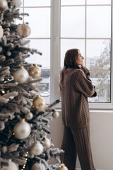 Woman looking out the window near a decorated Christmas tree