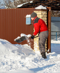 A man in a red jacket shovels snow off a building