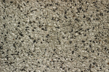 Texture of a grey stone wall with black and white speckles, featuring a rough surface