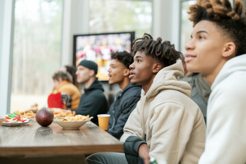 Friends watching Super Bowl football game eating snacks together at home