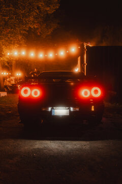 A Nissan Skyline GTR at night, its glowing taillights creating a striking silhouette under ambient lights. Perfect for themes of automotive luxury, performance, and iconic car design.