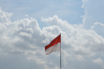 An Indonesian flag waving under a cloudy sky, symbolizing pride.