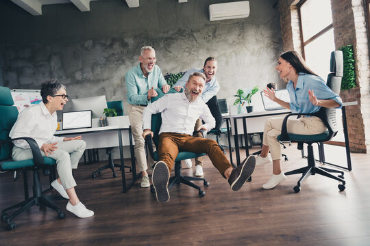Full body photo of teamwork people working together ride armchair have fun comfortable modern office loft room interior indoors workspace