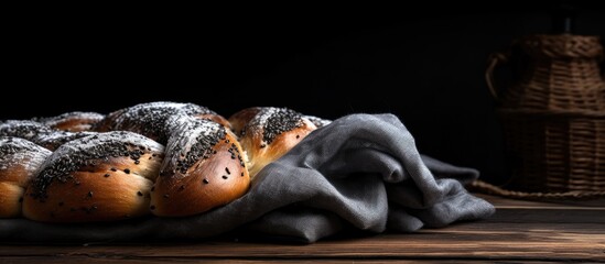 Freshly baked sweet braided bread with poppy seeds on dark wooden backdrop with grey fabric highlighting its texture and warmth