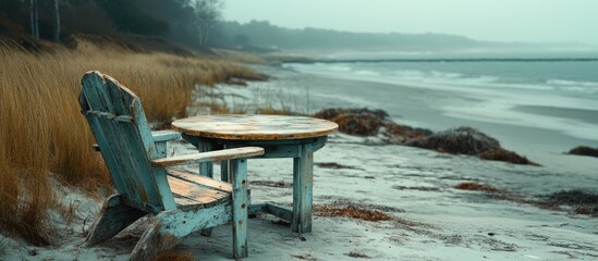 Rustic wooden table and beach chair overlooking a serene coastal landscape with misty shore and gentle waves in the background