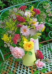 Still life of dahlias and roses, in metal jags on a rustic blue metal bench in a garden
