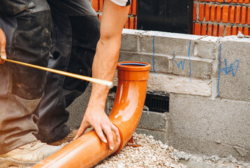 Builder installing a new plastic foul drainage pipe in a construction site during the day