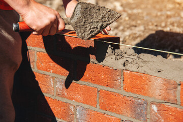 Bricklayer working on masonry project using trowel to apply mortar to bricks at construction site