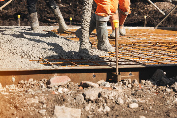 Naklejka premium Concreters pouring concrete on a building site while wearing safety gear in bright daylight