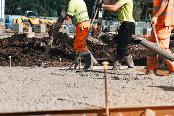 Workers pour concrete on construction site with heavy machinery in the background during sunny day