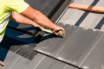 Skilled worker measures roofing materials during installation in a sunny outdoor setting