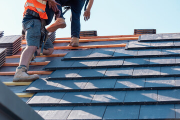 Skilled workers installing roofing tiles on a sunny day at a residential construction site