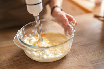 Mixing ingredients with a hand blender in a clear bowl on a wooden countertop in a bright kitchen