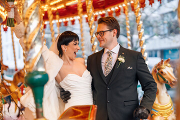 Joyful couple celebrating their wedding on a carousel in a festive outdoor setting during the daytime