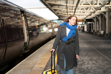 Woman with a suitcase walks along a train platform on a sunny day in a busy station during morning hours