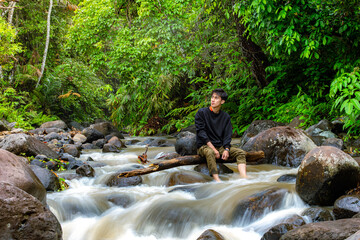 Man sitting on the river while looking around. Young man sitting alone in the middle of rain forest