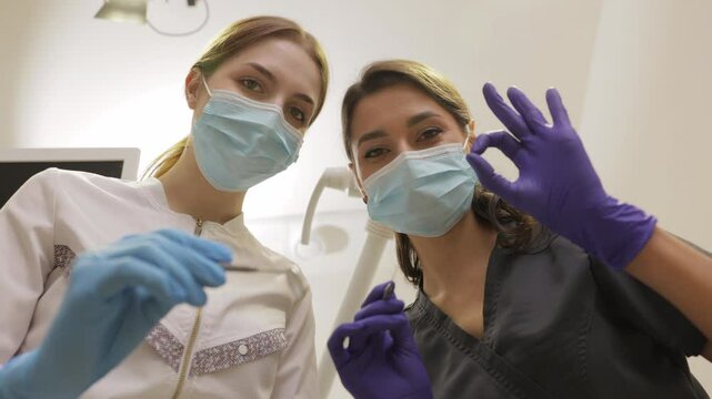 From below female dentists with mirror and device bending over patient during appointment in dental clinic