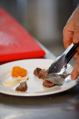 Chef is preparing a dish with meat, different sauces and pumpkin