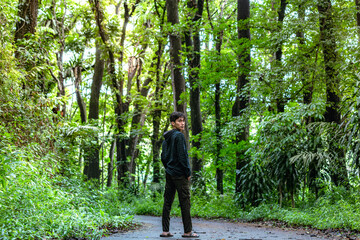 Young man standing alone while watching you. Beautiful dramatic deep forest greenery