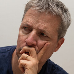 Obraz premium Close-up of a thoughtful middle-aged man with a furrowed brow, resting his face on his hand, reflecting deeply in a moment of concern