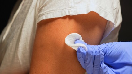 Healthcare worker using cotton and alcohol for cleaning patient shoulder skin before injecting...