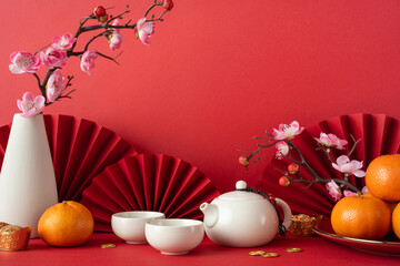White teapot and sakura blossoms with tangerines on a red background, symbolizing Chinese new year 2025 celebration