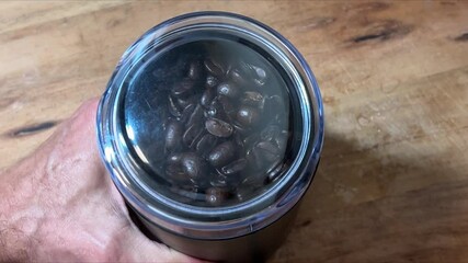 A coffee grinder machine on a piece of rustic wood griding some medium roasted coffee for breakfast. 