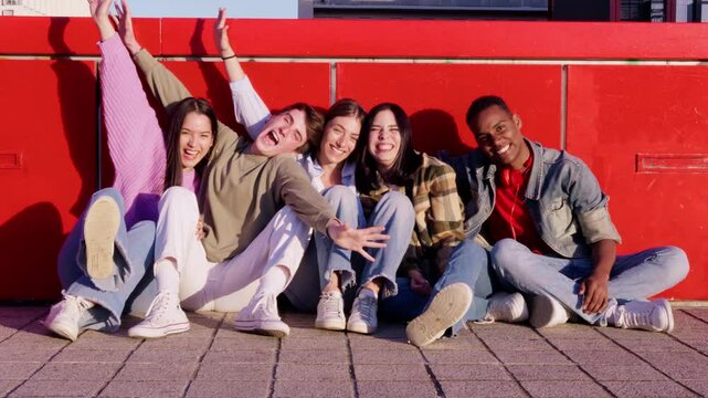 Teenagers sitting at the floor and spreading their arms over red background.