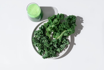 Batido de jugo de col rizada verde y hojas frescas de col rizada en un plato blanco sobre fondo...
