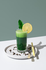 Jugo batido de espinacas adornado con una rodaja de limón sobre mesa blanca y fondo verde