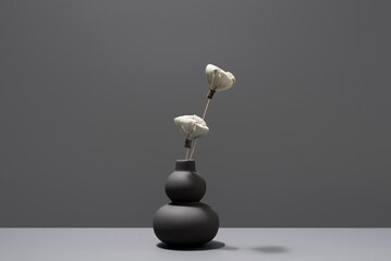 Flores secas blancas decorativas en un jarrón negro sobre fondo gris
