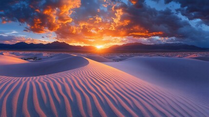 Vibrant sunset over white sand dunes and mountains.