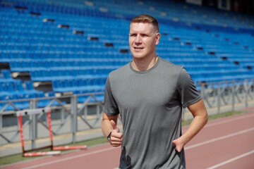 Athlete jogging on a track at an outdoor athletic stadium with empty stands in background during daytime training session