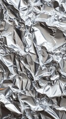 Close-up of crumpled silver foil reflecting light, creating an abstract metallic texture.