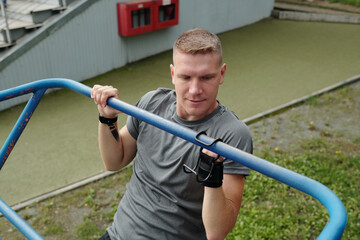 Man engaged in workout on outdoor horizontal bar showing determination and focus. Athlete's muscles are strained while gripping bars, highlighting dedication to fitness