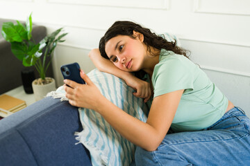 Teen girl feeling anxious while using her phone and waiting for a text message or reply