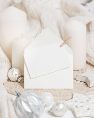 Card and envelope near white sweater, pillar candles and Christmas decor, mockup