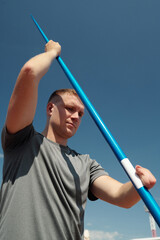 Athlete holding javelin while preparing for throw under clear sky. Javelin athlete wearing sports...