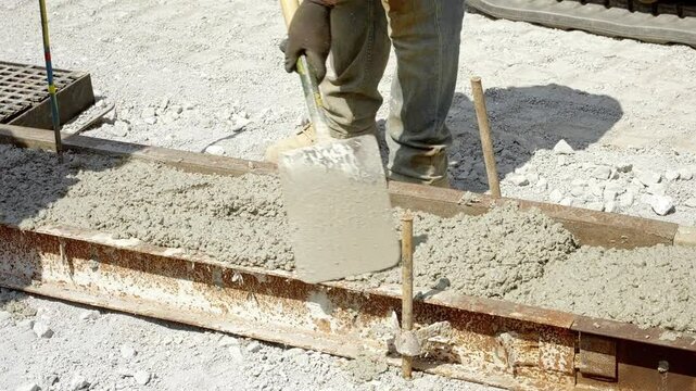 Construction worker pouring and leveling fresh concrete at a job site in bright sunlight