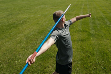 Athlete preparing to throw javelin while standing on green grass field. Showcasing technique and focus during outdoor sports activity