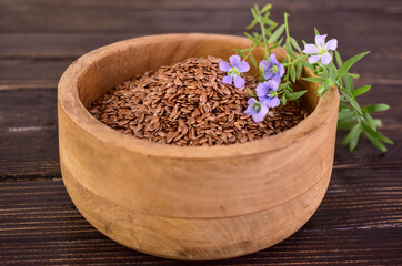 Flax seeds in a wooden bowl on a dark wooden background.
