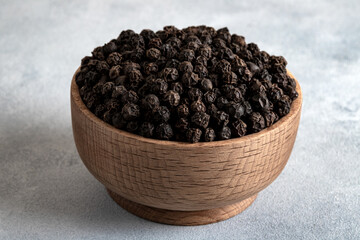 Black peppercorns in wooden bowl on light concrete background