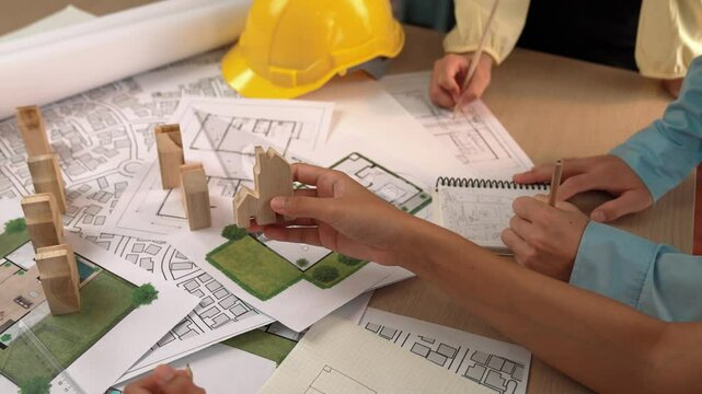 Architect and engineer consider or discuss about building construction using blueprint on table with architectural document, measurement tool and wooden block scatter around at office. Delineation.