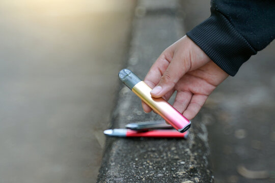 Hand holding an e-cigarette from a cement floor, concepts of types of cigarettes, harms and dangers, addictive substances.