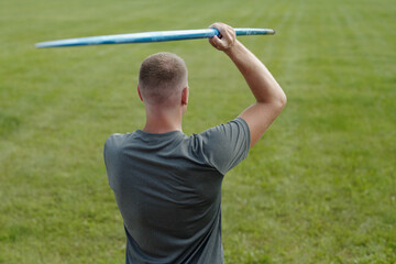 Man standing on open grassy field throwing frisbee with extended arm. Wearing casual grey t-shirt enjoying recreational activity on bright day