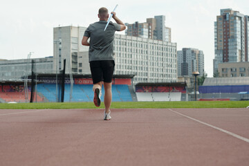 Obraz premium Athlete running at track while practicing javelin throw technique in city stadium with background of urban buildings during daytime offering dynamic sports action