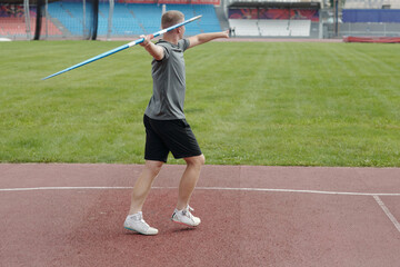 Athlete practicing javelin throw in outdoor athletic field. Person seen from behind, preparing for...