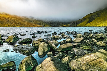 A misty mountain scene with a lake in the foreground and rolling hills in the background.