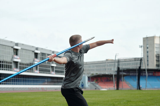 Athlete practicing javelin throw in sports complex, focusing on technique and form in preparation for competition. Background features grandstands and track